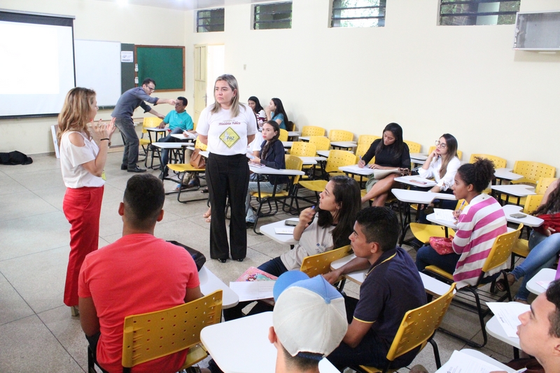 Duas pessoas de pé falando com as pessoas que estão sentadas 