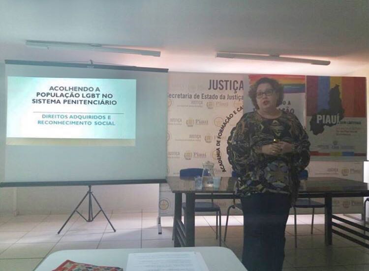 Mulher de pé falando em frente uma turma de pessoas que a assiste