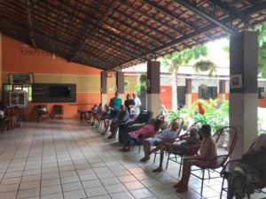 Pessoas sentadas com uma mulher ao fundo de pé