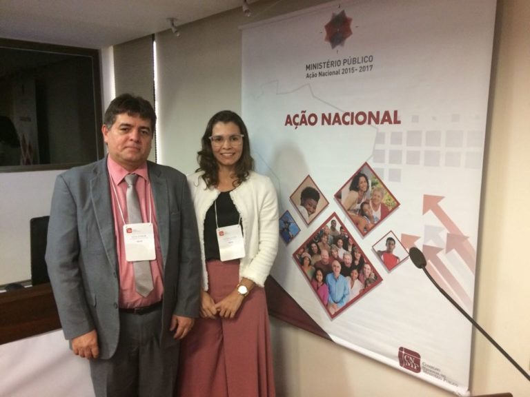 Duas pessoas ao lado de um cartaz sorrindo para fotografia