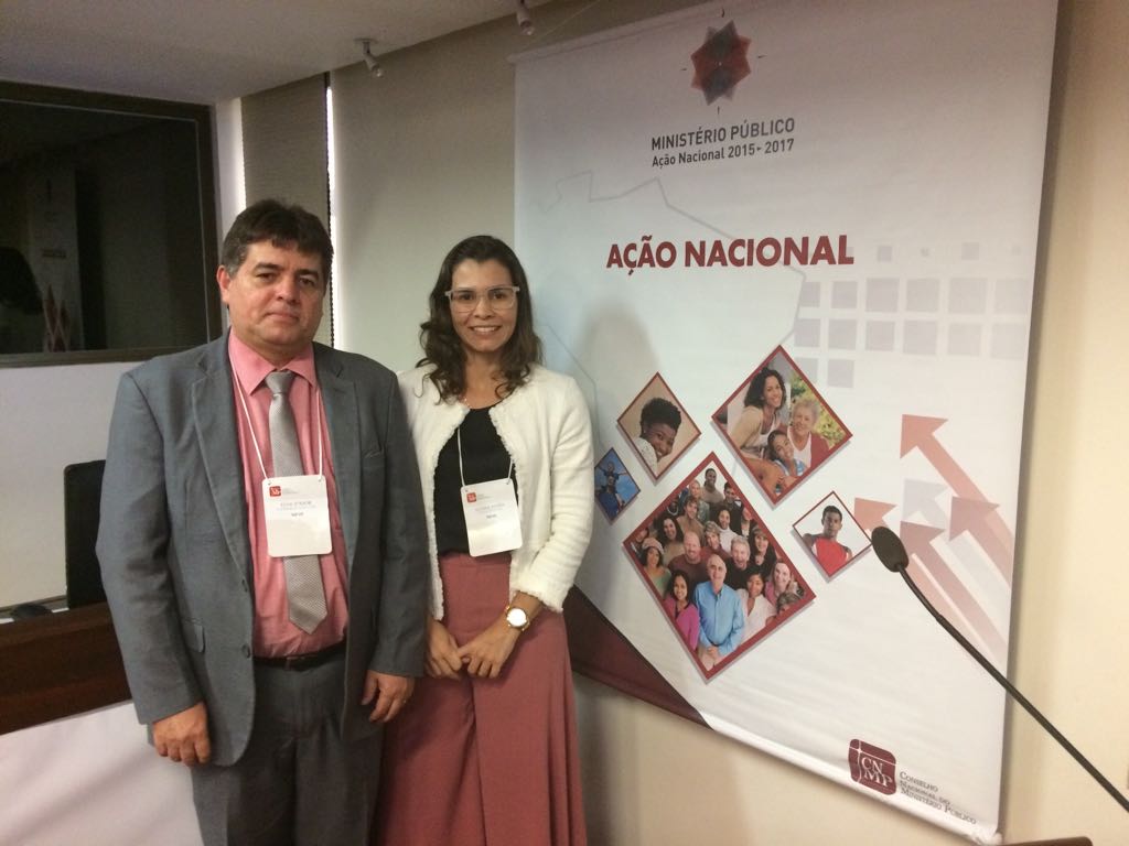 Duas pessoas ao lado de um cartaz sorrindo para fotografia 