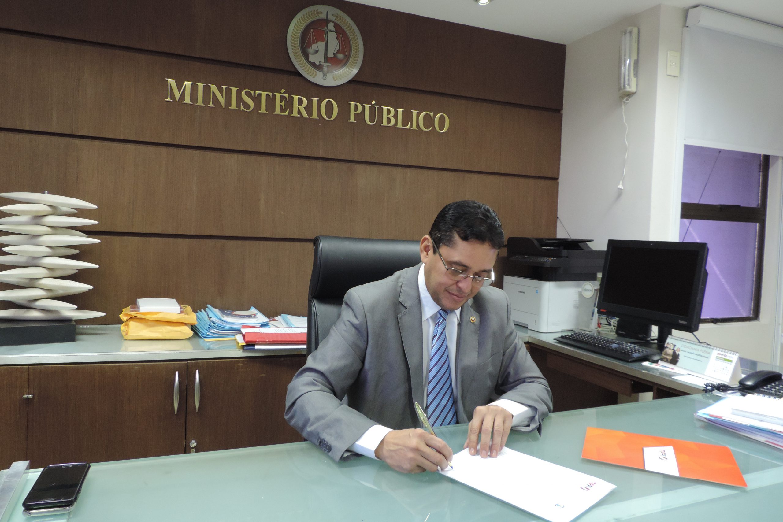 homem assinando papel que está sobre sua mesa 