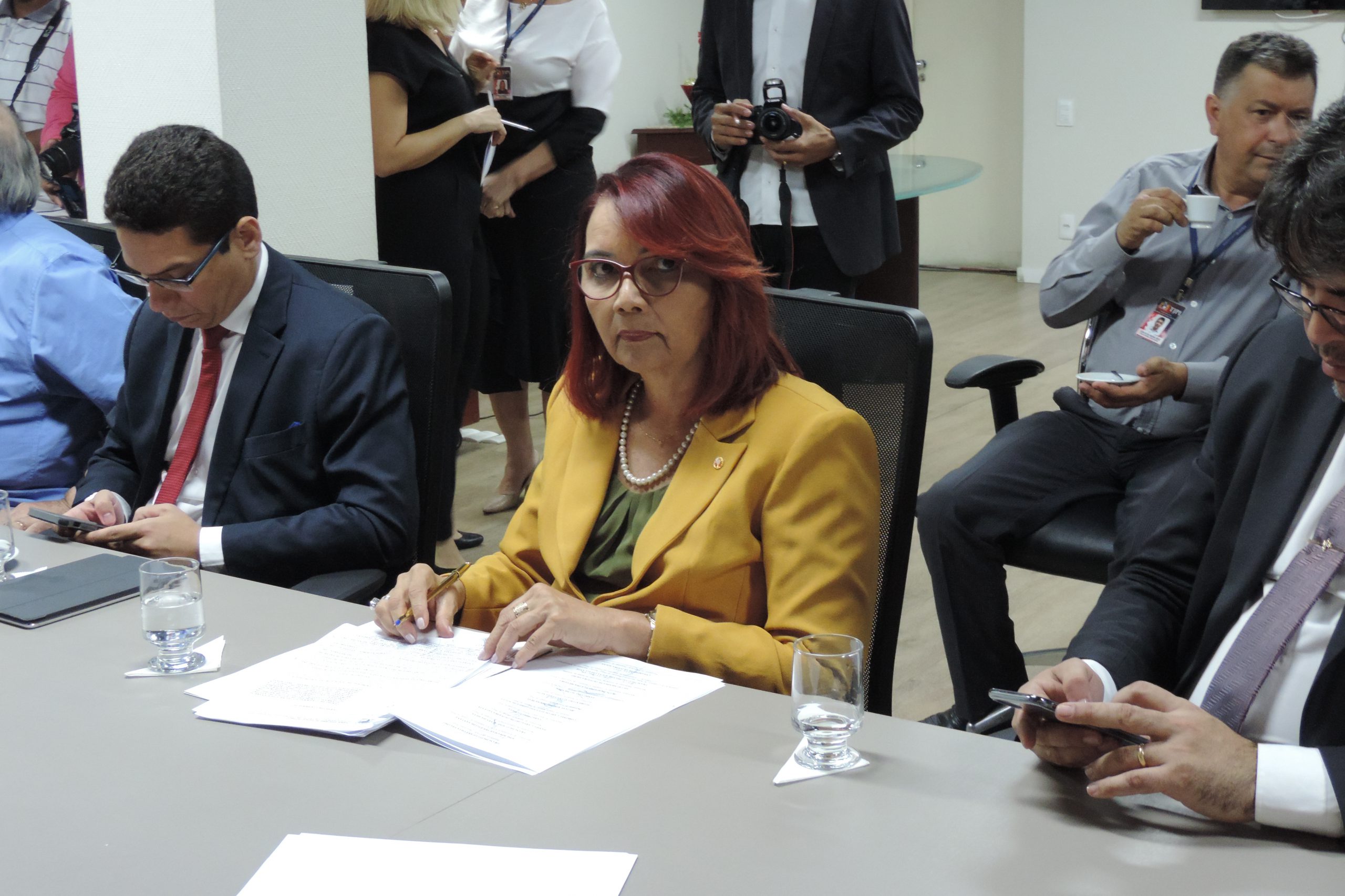 Mulher sentadas assinando um papel que está sobre a mesa 