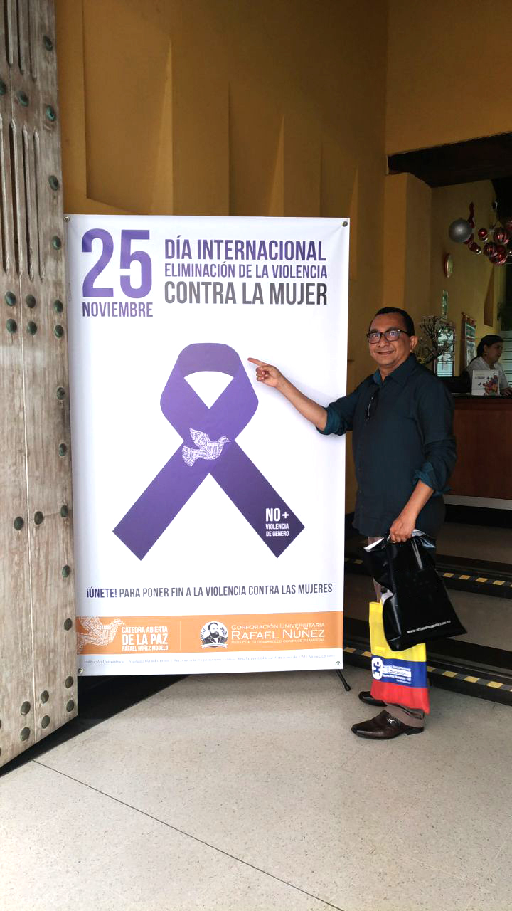 Pessoa de pé segurando sacolas com uma das mãos. Na outra aponta para o tema do evento no banner 