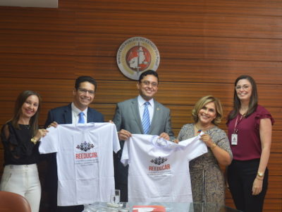 Equipes do MPPI e da SEJUS segurando camisas do projeto Reeducar