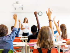 Crianças em sala de aula com as mãos levantadas