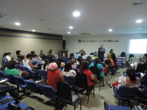 Pessoas sentadas em auditório vendo homem falar de pé