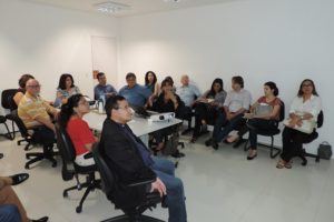 Pessoas sentadas em volta de uma mesa assistindo apresentação de um projeto