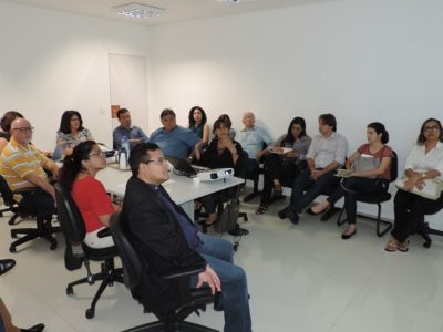 Pessoas sentadas em volta de uma mesa assistindo apresentação de um projeto