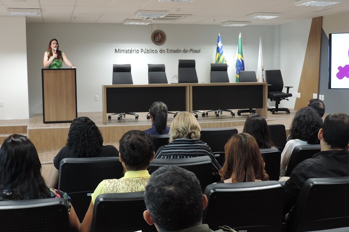 Pessoas sentadas em auditório observando mulher que fala 