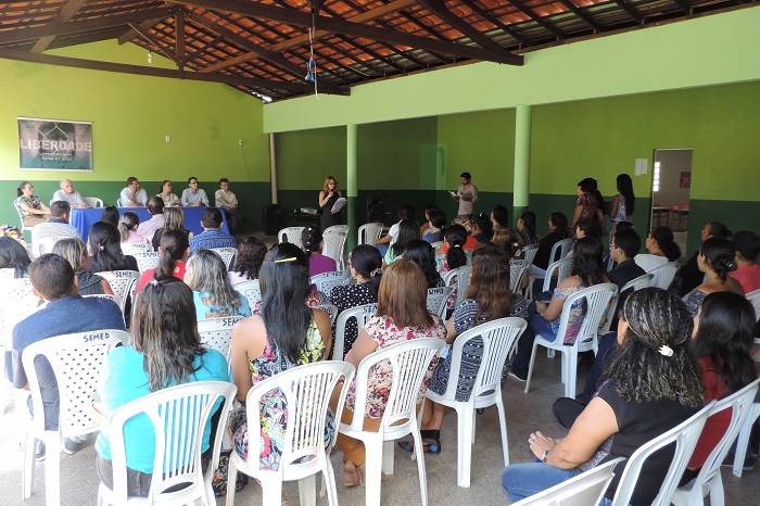 Pessoas sentadas observando mulher de pé discursando 