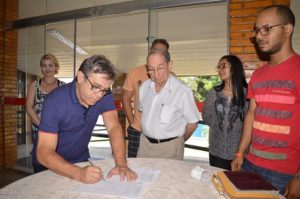 Homem assinando um papel e rodeado de pessoas