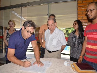 Homem assinando um papel e rodeado de pessoas