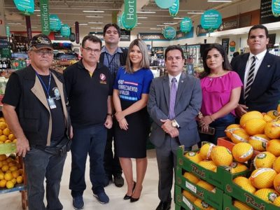Pessoas em pé entre frutas e verduras de um supermercado
