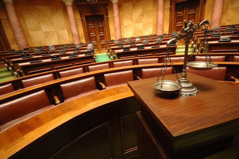 Foto de cadeiras ao fundo e a balança de justiça a frente