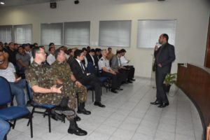 Pessoas sentadas observando um homem que está de pé falando para a plateia