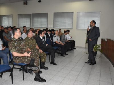 Pessoas sentadas observando um homem que está de pé falando para a plateia