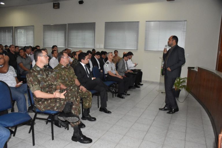 Pessoas sentadas observando um homem que está de pé falando para a plateia