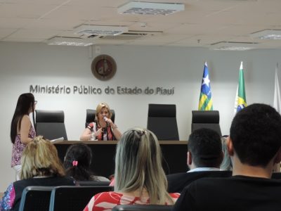 Pessoas sentadas observando uma mulher ao fundo