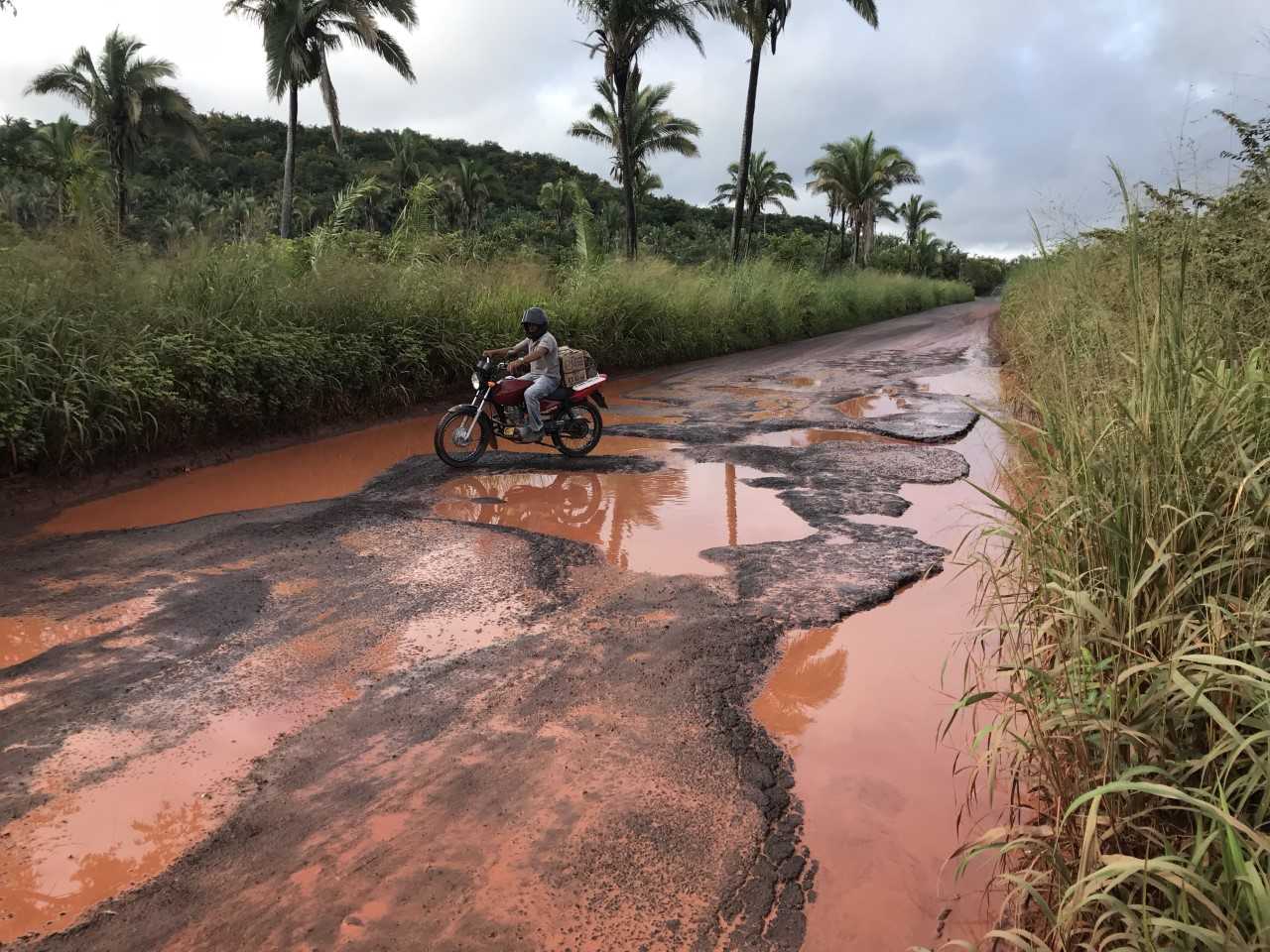 Rodovia em péssimas condições, com muitos buracos cheios de água