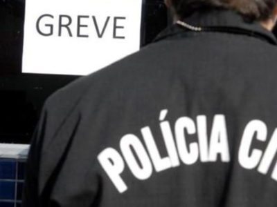 Imagem de policial civil de costas, diante de um cartaz de greve.