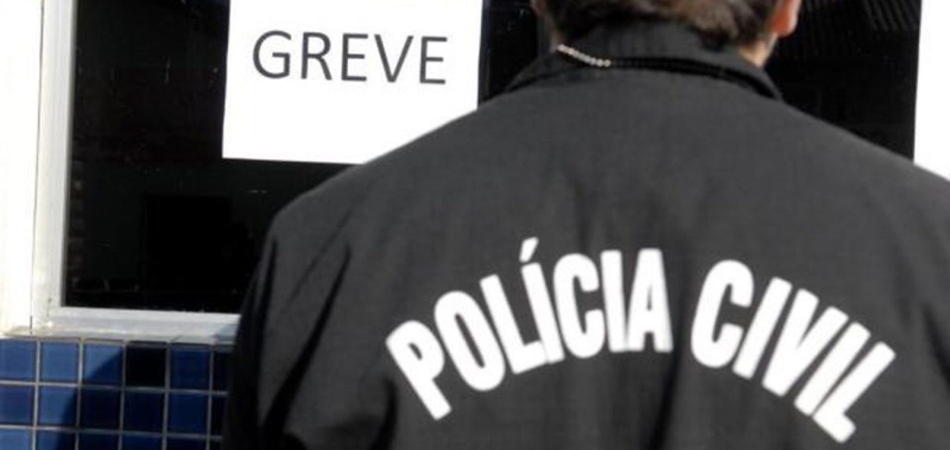 Imagem de policial civil de costas, diante de um cartaz de greve.