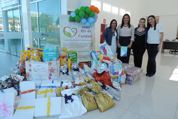 Pessoas de pé ao lado do donativos arrecadados com a campanha: Julho, Mês da Caridade