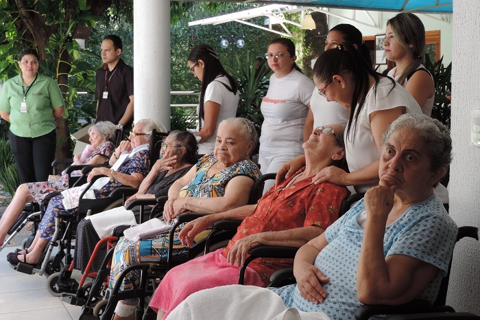 Idosas sentadas em cadeiras de rodas enquanto observam o evento de entrega do donativos da campanha Julho, Mês da Caridade 