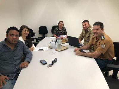 Pessoas sentadas em volta de uma mesa e sorrindo para a pessoa que está de pé em sua frente fazendo a fotografia