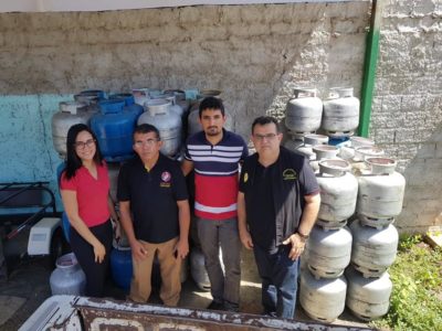 Quatro pessoas de pé rodeadas por botijões de gás