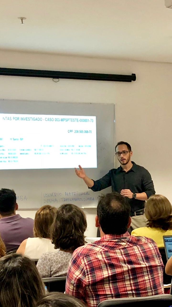 pessoas sentadas ouvindo um homem que está de pé. a cena ocorre dentro de uma sala de aula. 