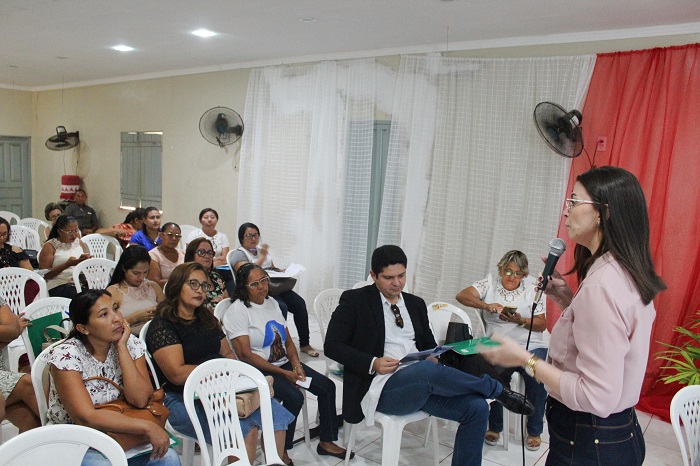 Pessoas sentadas em auditório vendo mulher de pé falar 