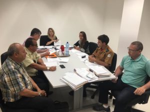 Pessoas sentadas em volta de uma mesa conversando durante reunião que resultou na assinatura de Termos de Ajustamento de Conduta