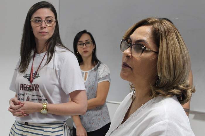 Fotos de mulheres que estão de pé. Uma delas olha para a outra que no momento fala com o público que participa do módulo do projeto Reeducar