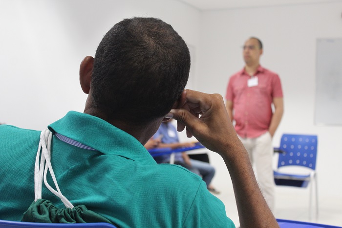 Homem sentado observando um outro homem que está de pé falando 