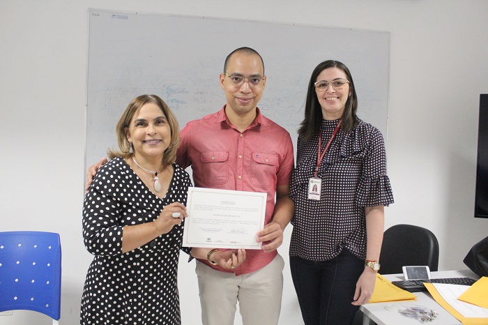 Três pessoas de pé sorrindo e segurando um certificado com as mãos 