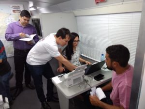 Pessoas sentadas em uma mesa sendo atendidas por servidores do PROCON