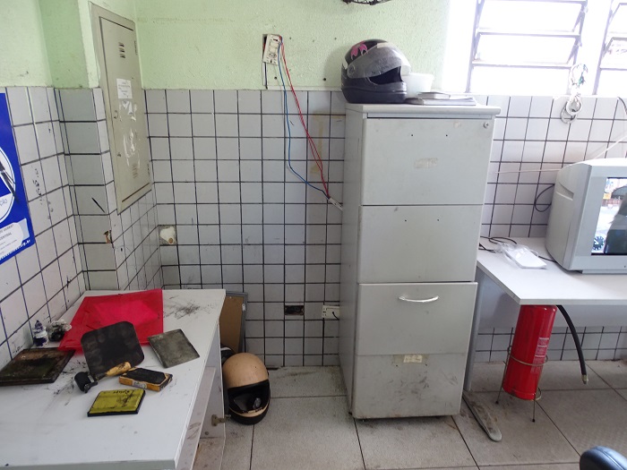 sala com objetos sujos em cima de mesa. Estante ao lado direito com fios passando por trás.