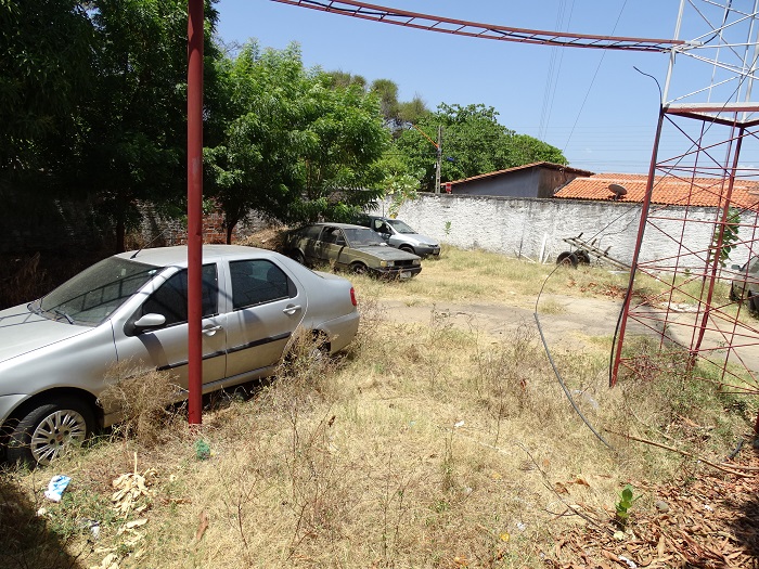 Pátio com carros estacionado e mato cobrindo até altura das rodas na Central de Flagrantes