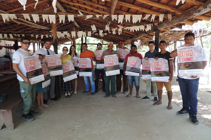 Pessoas de pe´segurando um cartaz que fala sobre os prejuízos que o fogo pode provocar 