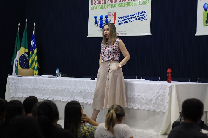 Mulher de pé conversando com a pessoas que a observam da plateia 