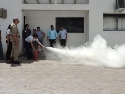 Pessoas de pé observando outra que manipula um extintor de incêndio