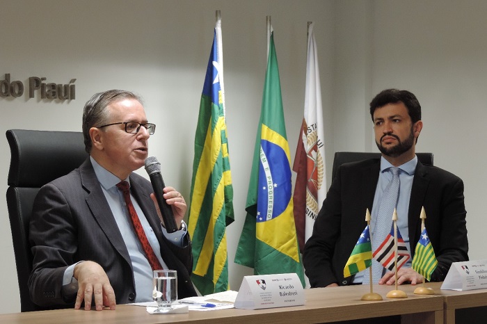 Dois homens sentados atrás de uma mesa 