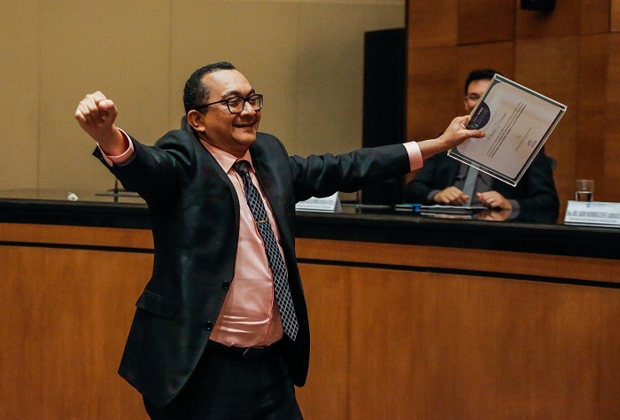 HOmem de braços abertos segurando um papel e sorrindo 