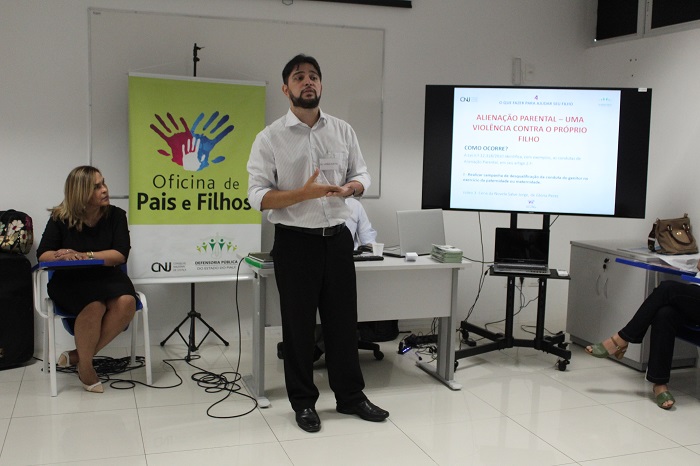 Homem de pé falando para o público que o assiste 