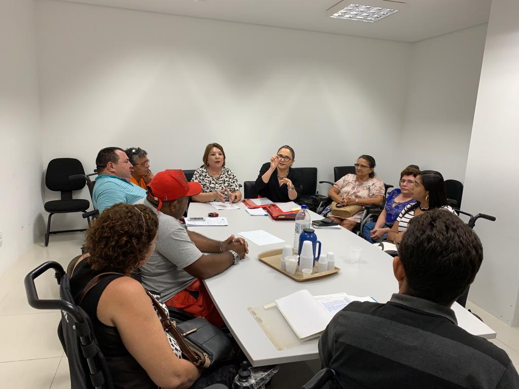 Grupo de pessoas sentadas à mesa observando uma pessoa falar