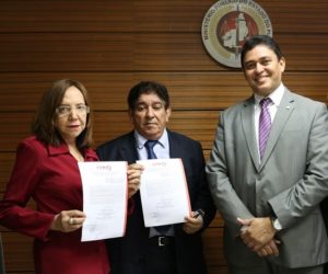Três pessoas de pé, duas seguram um documento em suas mãos