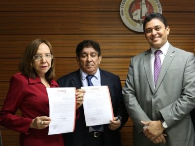 Três pessoas de pé, duas seguram um documento em suas mãos