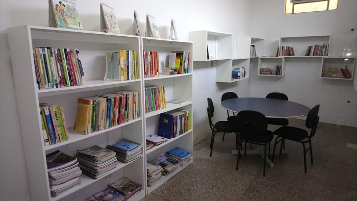 Fotos da estrutura da biblioteca. No espaço estão mesas, estantes, cadeiras e os livros obtidos com as doações