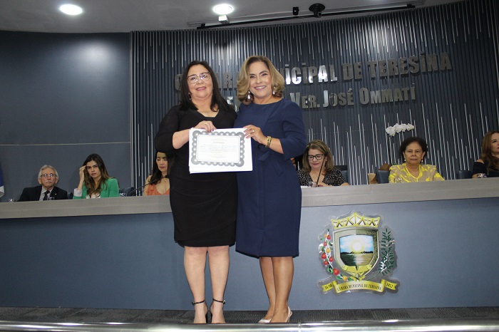 Duas mulheres de pé segurando um diploma e sorrindo para a fotografia